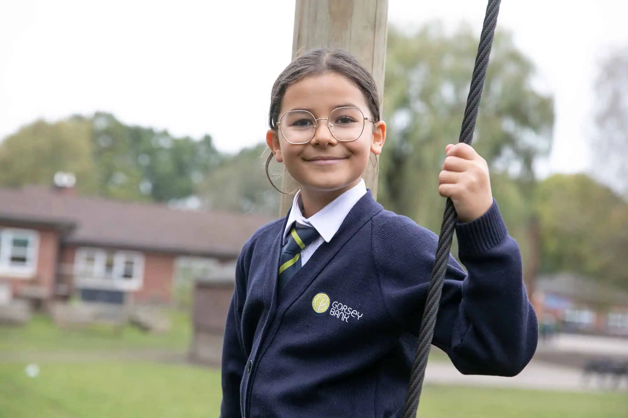 A pupil at Gorsey Bank smiles while holding a rope on an outdoor adventure play area.